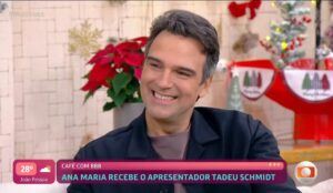 Tadeu Schmidt sorrindo durante entrevista no programa “Mais Você”, ao lado de enfeites natalinos, enquanto fala sobre o BBB 26.