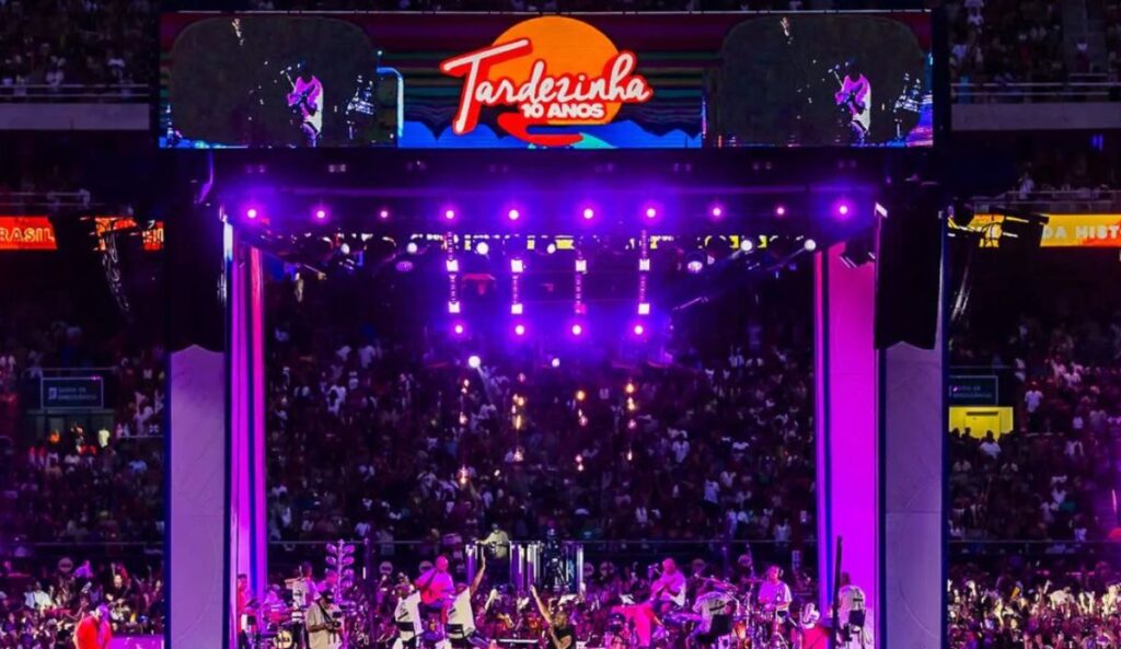 Palco 360º da Tardezinha 10 anos lotado durante show de Thiaguinho, com público em estádio e iluminação roxa.