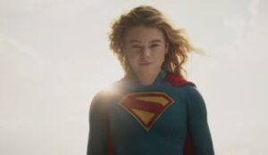 Cena de “Supergirl”: Milly Alcock aparece caracterizada como a heroína, usando o uniforme azul e vermelho com o símbolo do Superman no peito, iluminada pelo sol ao fundo.
