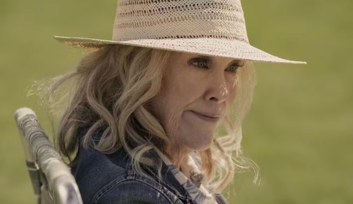 Catherine O’Hara em cena dramática, usando chapéu e jaqueta, em uma de suas últimas atuações na televisão.