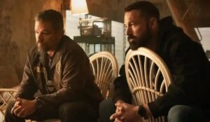 Cena do filme Dinheiro Suspeito: dois policiais sentados em cadeiras de vime dentro de um galpão abandonado, em clima tenso, durante investigação envolvendo dinheiro ilícito.