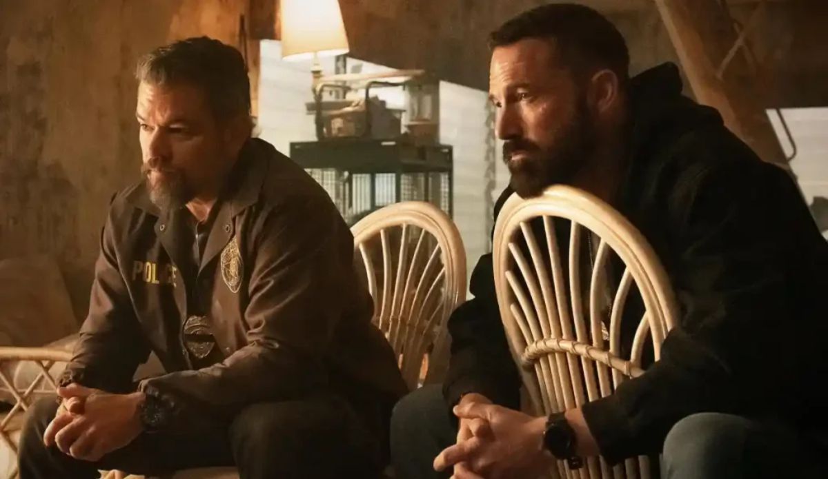 Cena do filme Dinheiro Suspeito: dois policiais sentados em cadeiras de vime dentro de um galpão abandonado, em clima tenso, durante investigação envolvendo dinheiro ilícito.