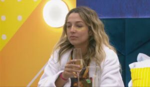 Samira, Líder do BBB 26, sentada à mesa segurando uma taça de espumante durante conversa na casa