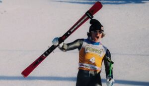 Lucas Pinheiro Braathen, atleta de esqui alpino celebra na neve erguendo os esquis durante prova; ele está presente nos Jogos Olímpicos de Inverno 2026.