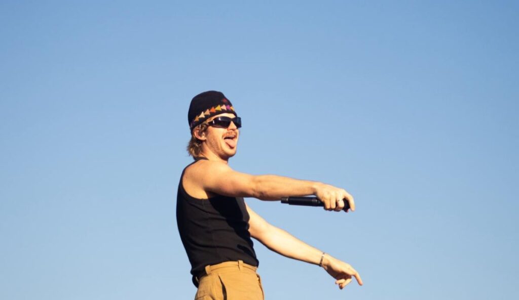 Djo se apresenta no Lollapalooza Brasil 2026, cantando no palco Budwaiser ao ar livre com microfone e céu azul ao fundo