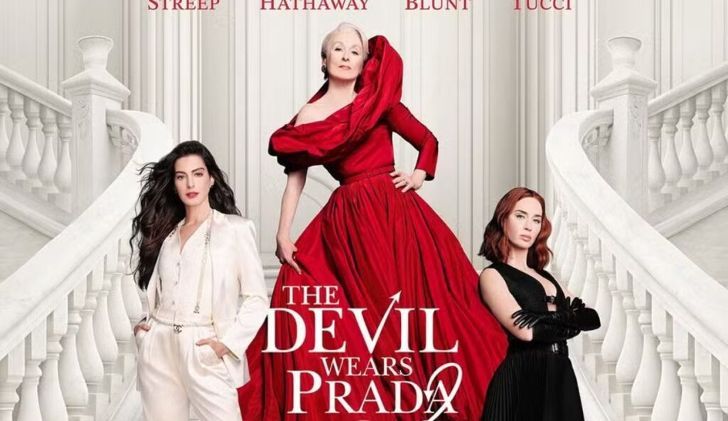 Meryl Streep, Anne Hathaway e Emily Blunt aparecem em escadaria elegante no pôster de “O Diabo Veste Prada 2”, com Miranda Priestly em vestido vermelho no centro, destacando o retorno do elenco na sequência do filme.