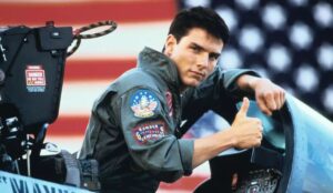 Tom Cruise como Maverick em Top Gun: Ases Indomáveis durante cena icônica com uniforme de piloto e avião ao fundo