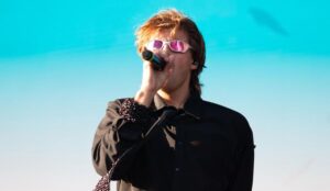 Ruel canta no Lollapalooza Brasil 2026 usando roupa preta e óculos escuros diante de céu azul no palco