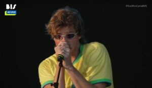Ruel durante apresentação no Lollapalooza Brasil 2026, usando camisa amarela da seleção brasileira e óculos escuros enquanto canta no palco