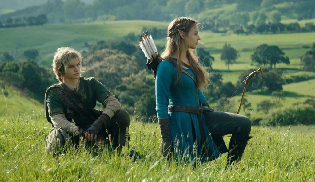 Cena do filme live-action de The Legend of Zelda mostra Link e a Princesa Zelda em um campo aberto, com roupas medievais e arco e flecha, observando a paisagem ao redor.