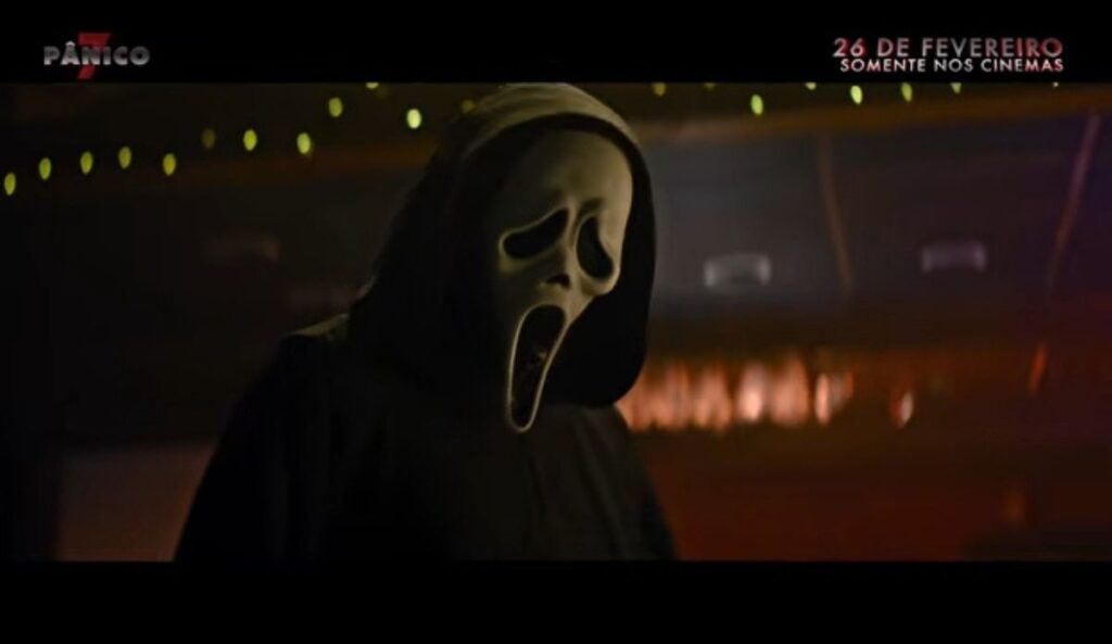 Ghostface em cena de Pânico 7, usando máscara clássica e capuz preto em ambiente escuro e iluminado, em imagem do trailer oficial do filme de terror