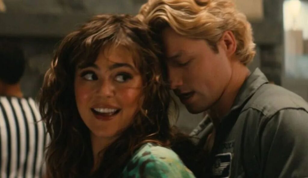 **Alt text:** Allie e Dean aparecem sorrindo e próximos em cena da série “Off Campus”. A personagem olha para ele enquanto o jovem se inclina em direção ao rosto dela em um momento romântico.