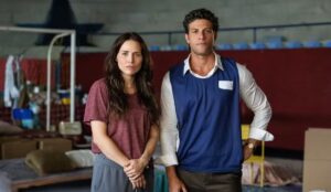 Leticia Colin e Chay Suede em cena de “Quem Ama Cuida”, nova novela da Globo. Os personagens aparecem lado a lado dentro de um abrigo improvisado, em um momento de tensão da trama.