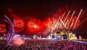 Imagem de divulgação do Palco Mundo do Rock in Rio, com multidão na Cidade do Rock e queima de fogos durante apresentação ao vivo.