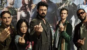 Elenco principal de “The Boys” reunido em imagem promocional da temporada final da série do Prime Video. Os personagens aparecem fazendo gesto obsceno diante de pôsteres dos heróis da Vought.