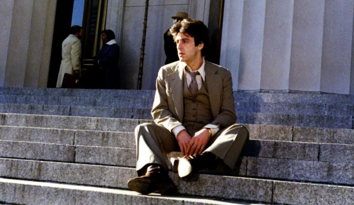 Al Pacino em cena do filme “Justiça para Todos” (1979), drama jurídico que ganhará adaptação em série pela Netflix. O ator aparece sentado nos degraus de um tribunal, usando terno bege e expressão pensativa.