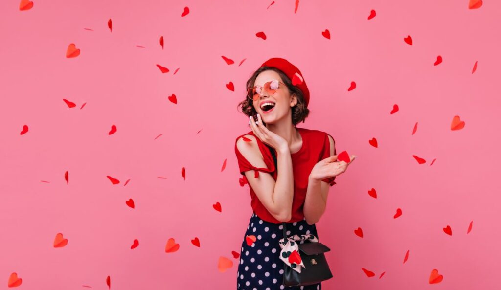 Mulher sorridente em cenário rosa com corações vermelhos para playlist de músicas do Dia dos Namorados.