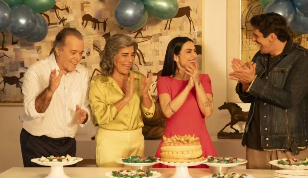Glória Pires, Tony Ramos, Cleo e Rafael Infante aparecem reunidos em cena de “Se Eu Fosse Você 3”, celebrando em frente a uma mesa com bolo, doces e balões.