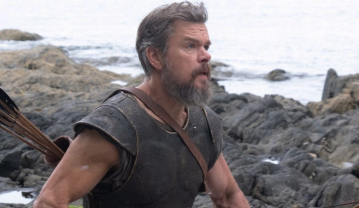 Matt Damon caracterizado como Odisseu em cena de "A Odisseia", filme dirigido por Christopher Nolan. O ator aparece em uma praia rochosa usando traje de guerreiro.