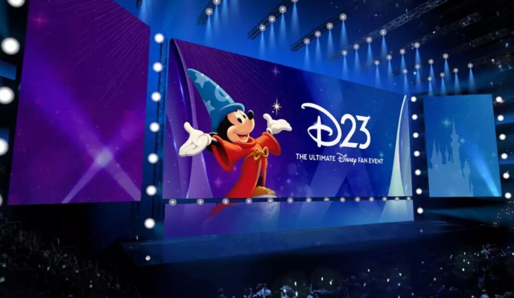 Palco da D23 com telões iluminados em azul e roxo, exibindo o Mickey como aprendiz de feiticeiro e o logotipo do evento de fãs da Disney.